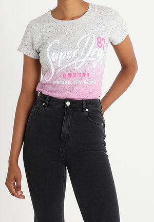 Personne portant un t-shirt gris et rose Superdry 87 vintage, marque japonaise, rentré dans un jean noir taille haute.