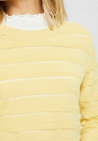 Keltainen neulepusero, jossa vaakasuorat raidat ja avoneulekuvioinnit. Pyöreä pääntie ja resorit helmassa. Pehmeä materiaali, rento malli.