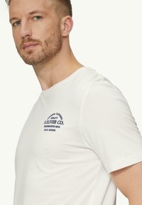 Weißes Baumwoll-T-Shirt mit kurzen Ärmeln und rundem Halsausschnitt. Die Vorderseite zeigt dunkelblaue gedruckte Texte und ein Logo in einem Bogen-Design.