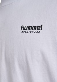 Balts kokvilnas T-kreklis ar melnu apdrukātu logo, kas priekšpusē lasāms "hummel SPORTSWEAR". Gluda tekstūra, ar apaļu kakla izgriezumu.