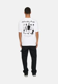 White t-shirt with a graphic print on the back featuring black-and-white figures, paired with black cargo pants and sneakers.
