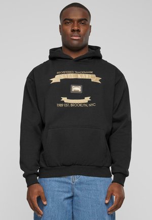 Black hoodie featuring a gold graphic with "KARL KANI" and a trademark label. It has a front pocket and ribbed cuffs and hem.