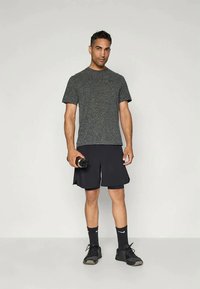 Szürke sportpóló, fekete rövidnadrág részekkel, fekete zoknik és sportcipők. Vízszerelőt tart a kezében. Egyszerű, funkcionális sportöltözet dizájn.