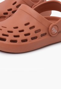 Orange rubber clogs featuring ventilation holes, a curved silhouette, and an adjustable strap with a circular logo accent.