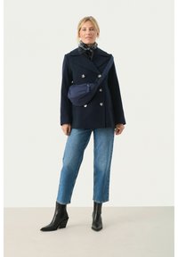 Marinblå dubbelknäppt kappa med silverbrytare, blå mönstrad scarf, avslappnade ljusblå jeans och svarta ankelstövlar med klack.