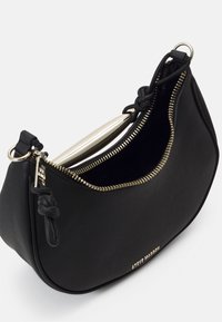 Sac à main noir en forme de croissant avec fermeture éclair dorée partiellement ouverte, détails de sangle nouée et petit logo doré "Steve Madden" à l'avant.