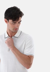 Weißes Kurzarm-Polohemd mit kragenähnlichem Ausschnitt und schwarzen Akzentstreifen, hergestellt aus leichtem, strukturiertem Stoff.