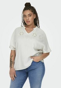 Hvid kortærmet top med en tekstureret overflade, der har broderede blomsterdetaljer ved halsudskæringen, parret med blå jeans.