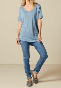 Lichtblauw V-hals T-shirt met korte mouwen, gecombineerd met nauwsluitende blauwe jeans en zwarte slip-on schoenen met een patroon. Gladde stof, ontspannen pasvorm.