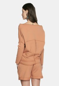 Pomarańczowy sweter z szerokim dekoltem, długimi rękawami i detalami szwów, w połączeniu z pasującymi szortami. Gładka tekstura, casualowy design.