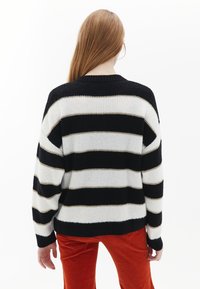Svart och vit randig tröja med avslappnad passform, strukturerat stickat tyg, ribbade ärmslut och rund halsringning, sedd bakifrån.