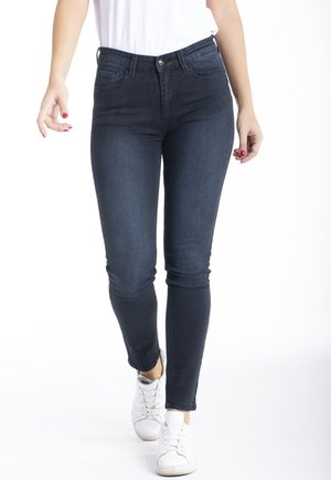 Jean skinny bleu foncé en denim, avec une taille mi-haute, un design classique à cinq poches, une texture lisse et un minimalisme dans les détails.