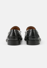 Schwarze Lackleder-Slipper mit glatter Oberfläche, abgerundeter Zehe und niedrigem Absatz. Verfügt über dekorative Nähte im Obermaterial.