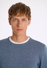 Μπλε πλεκτό πουλόβερ με στρογγυλή λαιμόκοψη και λευκή εσωτερική γιακά. Διαθέτει υφασμάτινη υφή και διακριτική λεπτομέρεια με λογότυπο στο στήθος.