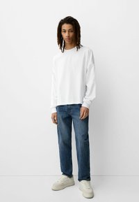 Camicia bianca a maniche lunghe con una vestibilità comoda, abbinata a jeans in denim blu e sneakers color crema; design minimale, tessuto morbido.