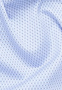 Hellblaues Gewebe mit einem kleinen geometrischen Muster aus ineinandergreifenden Kreisen und Rauten, das natürliche Falten und Textur zeigt.