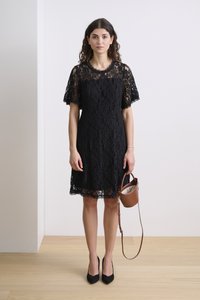 Black lace dress with short sleeves and a round neckline, paired with a small brown handbag. High-heeled black shoes.