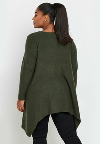 Långärmad, mörkgrön stickad tunika med asymmetrisk nederkant, mjuk struktur och rund halsringning. Har enkla, rena linjer och inga dekorationer.