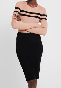 Robe en tricot côtelé de deux couleurs : pêche avec des rayures noires sur les manches, se transformant en une jupe noire ajustée. Manches longues, encolure ronde.