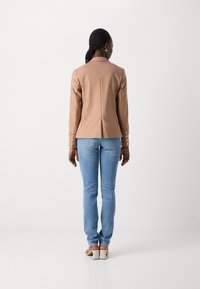 Beige umělá kožená blejzr s propracovaným designem, s jedním rozventilováním a knoflíkovými detaily na rukávech, doplněný o světle modré skinny džíny.