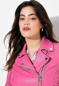 Fuchsia Leder-Motorradjacke mit silbernen Reißverschlüssen und Druckknöpfen. Darunter ist eine mehrfarbige gemusterte Bluse teilweise sichtbar.