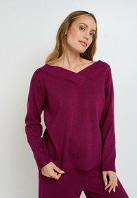 Pullover a V-collo in magenta profondo, con maniche lunghe e una maglia morbida e testurizzata. Finitura liscia con un leggero luccichio in tutto il capo.