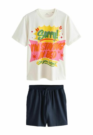 Weißes Kurzarmhemd mit buntem Text "Sorry! Ich bleibe im Bett, bis später!" kombiniert mit einfachen schwarzen Shorts mit elastischem Bund.