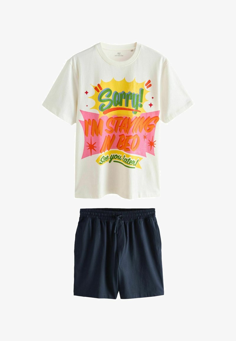 Hvid kortærmet skjorte med farverig tekst "Undskyld! Jeg bliver i sengen, vi ses senere!" kombineret med ensfarvede sorte shorts med elastik i taljen.
