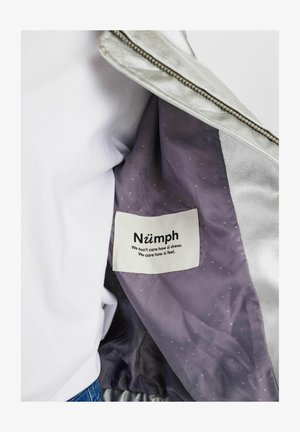 Srebrna, metaliczna kurtka o gładkiej powierzchni. Wnętrze wykończone jest fioletową podszewką w kropeczki oraz metką z tkaniny z nazwą marki.