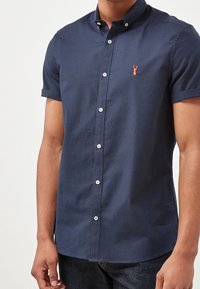 Camisa de algodón de manga corta en color navy con cuello abotonado, botones blancos y un pequeño logo de langosta bordado en el pecho.