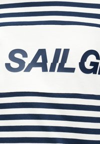 Ύφασμα με οριζόντιες ριγέ σε ναυτικό μπλε και λευκό, με έντονο ναυτικό μπλε κείμενο που διαβάζεται μερικώς "SAIL G" στο κέντρο.