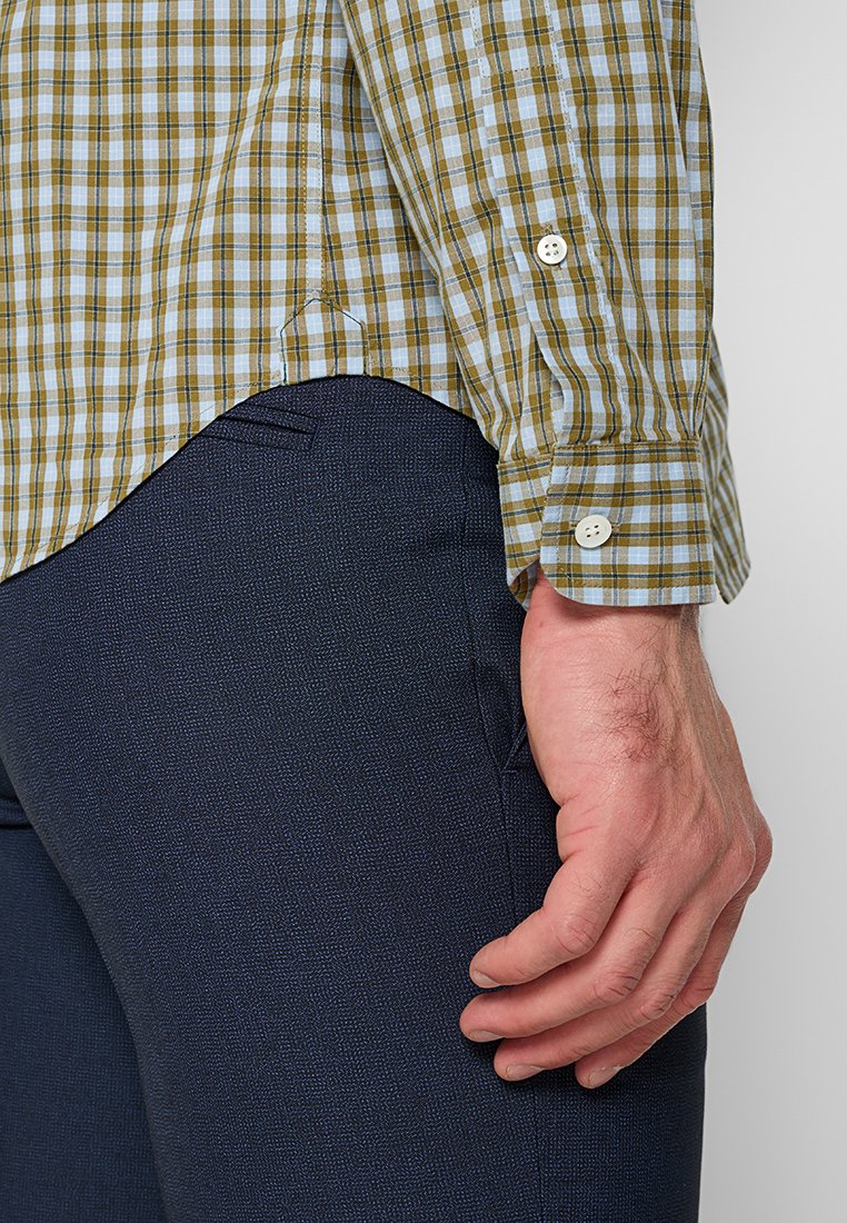 Karierter Hemd in Beige- und Blautönen, aus einem Stoff mit glatter Textur. Verfügt über verstellbare Manschetten und einen geschwungenen Saum. Dunkle Hose mit einem dezenten Muster.