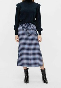 Black knit sweater with long sleeves paired with a blue and black plaid midi skirt featuring a tied waist and side slit. Black heeled boots.