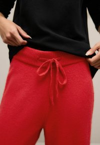 Rode gebreide sweatpants met een geribde tailleband en trekkoorddetail, gecombineerd met een zwarte top, die een zachte textuur en een ontspannen pasvorm tonen.