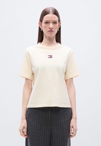 Κίτρινο ανοιχτό κοντομάνικο μπλουζάκι με στρογγυλή λαιμόκοψη, με μικρό ορθογώνιο λογότυπο σε κόκκινο, άσπρο και μπλε στο στήθος. Επίπεδη υφή.