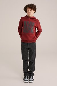 Raudona gobtuvinė džemperis su juodu tekstu "BLUE RIDGE DENIM", derinama su tamsiomis džinsomis ir juodais sportbačiais. Kasdienis stilius su raibu rankogaliais.