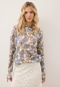 Bloemige gebreide trui met blauwe en groene patronen, ronde halslijn, geribde manchetten en een relaxte pasvorm, gecombineerd met een witte kanten rok.