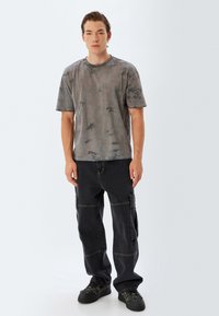 Grå tie-dye bomulds t-shirt med korte ærmer parret med sorte cargo bukser med lommer og kontrastsyninger; sorte sneakers fuldender looket.