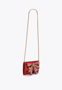Borsa a tracolla in pelle verniciata rossa con un elegante fiocco decorato con gioielli, tracolla in catena dorata e forma rettangolare compatta. Finitura lucida e testurizzata.