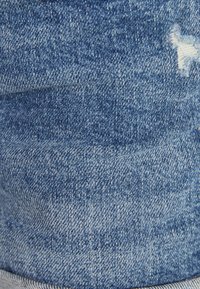 Primer plano de una tela de denim azul con un pequeño desgarro desgastado que muestra hilos blancos en la esquina superior derecha.
