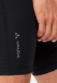 Shorts de sport noirs en matériau extensible, avec le logo embossé "Vaude" sur le côté gauche, une coupe ajustée et des coutures visibles.