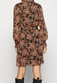 Musta pitkähihaine mekko, jossa on oranssi ja kerma väreissä kukkakuosi. Mekossa on kerätty hihansuu ja vyötä ympäröivä muotoilu, joka luo flare-mallisen hameen siluetin.