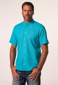 Camicia corta manica turchese con colletto alla cinese, caratterizzata da bottoni bianchi, una vestibilità rilassata e una texture liscia. Indossata con jeans.