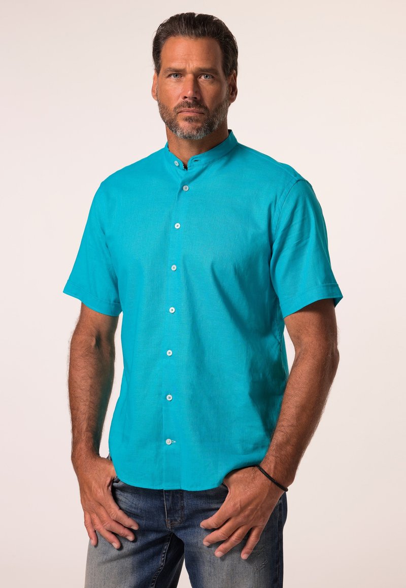 Camicia corta manica turchese con colletto alla cinese, caratterizzata da bottoni bianchi, una vestibilità rilassata e una texture liscia. Indossata con jeans.