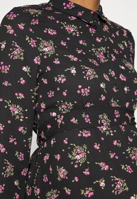 Vestido preto com padrão floral, apresentando flores cor-de-rosa e detalhes em verde; gola com botões, cintura franzida e textura de tecido suave.