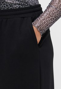Melns audums ar gludu tekstūru, ar sānu kabatu. Piedurknei ir spīdīgs leopardu raksts pelēkā un melnā krāsā.