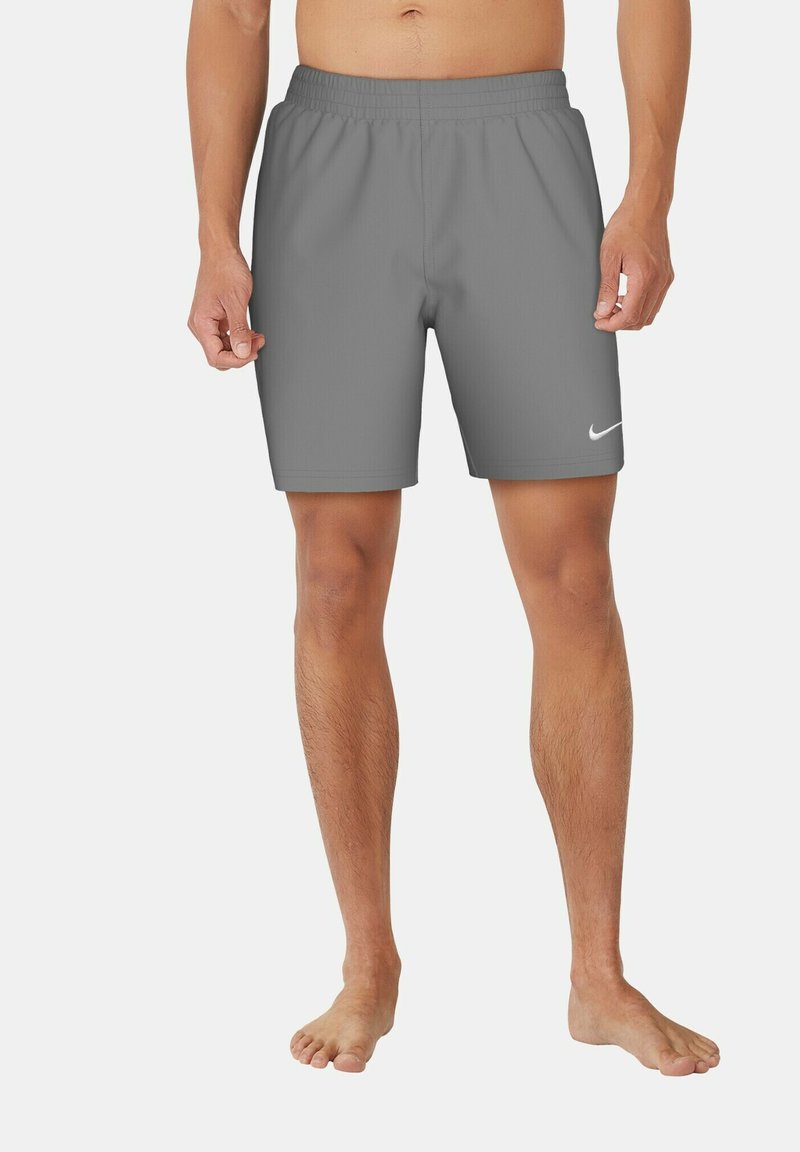 Άνδρας που φοράει γκρι αθλητικά σορτς Nike με ελαστική μέση, στέκεται ξυπόλυτος σε απλό φόντο.