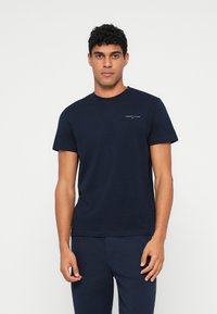 Tengerészkék pamut póló kerek nyakkal és rövid ujjakkal. Kis fehér logó a bal mellrészen. Sima, mintázat nélküli fazon.