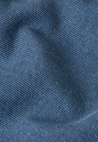 Detailní pohled na texturovanou modrou látku s viditelným pleteným vzorem a jemnými záhyby, které vytvářejí hloubku a stín.