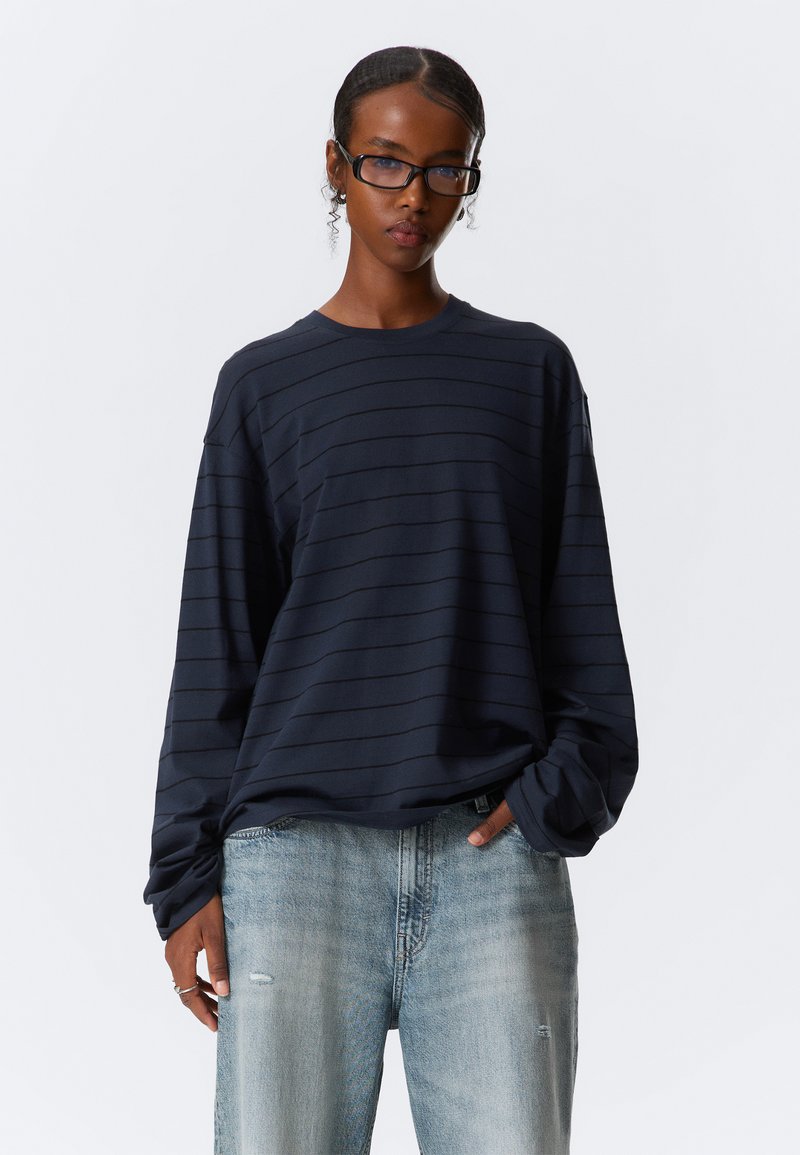 Μπλε ναυτικό μπλουζάκι με μακριά μανίκια και οριζόντιες ρίγες, στρογγυλή λαιμόκοψη, άνετη γραμμή, συνδυασμένο με ανοιχτό μπλε τζιν με σκισίματα.